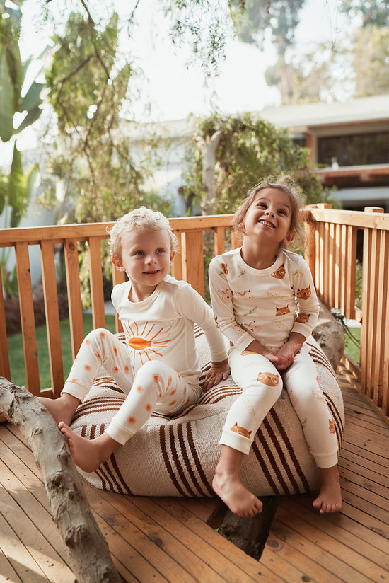 Two kids in comfortable Rising Sun and Cozy Boho Tiny Otters children's pajamas enjoying their time outside on a deck