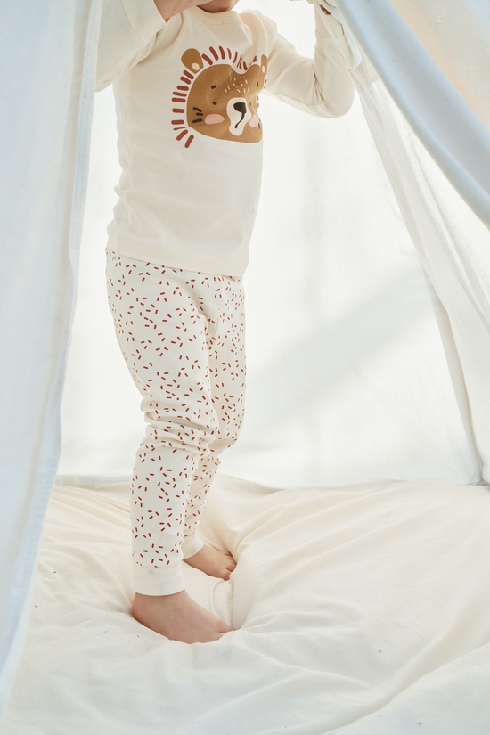 A child in comfortable Dreamy Lion Tiny Otters childrens pajamas standing and hiding behind a bedsheet