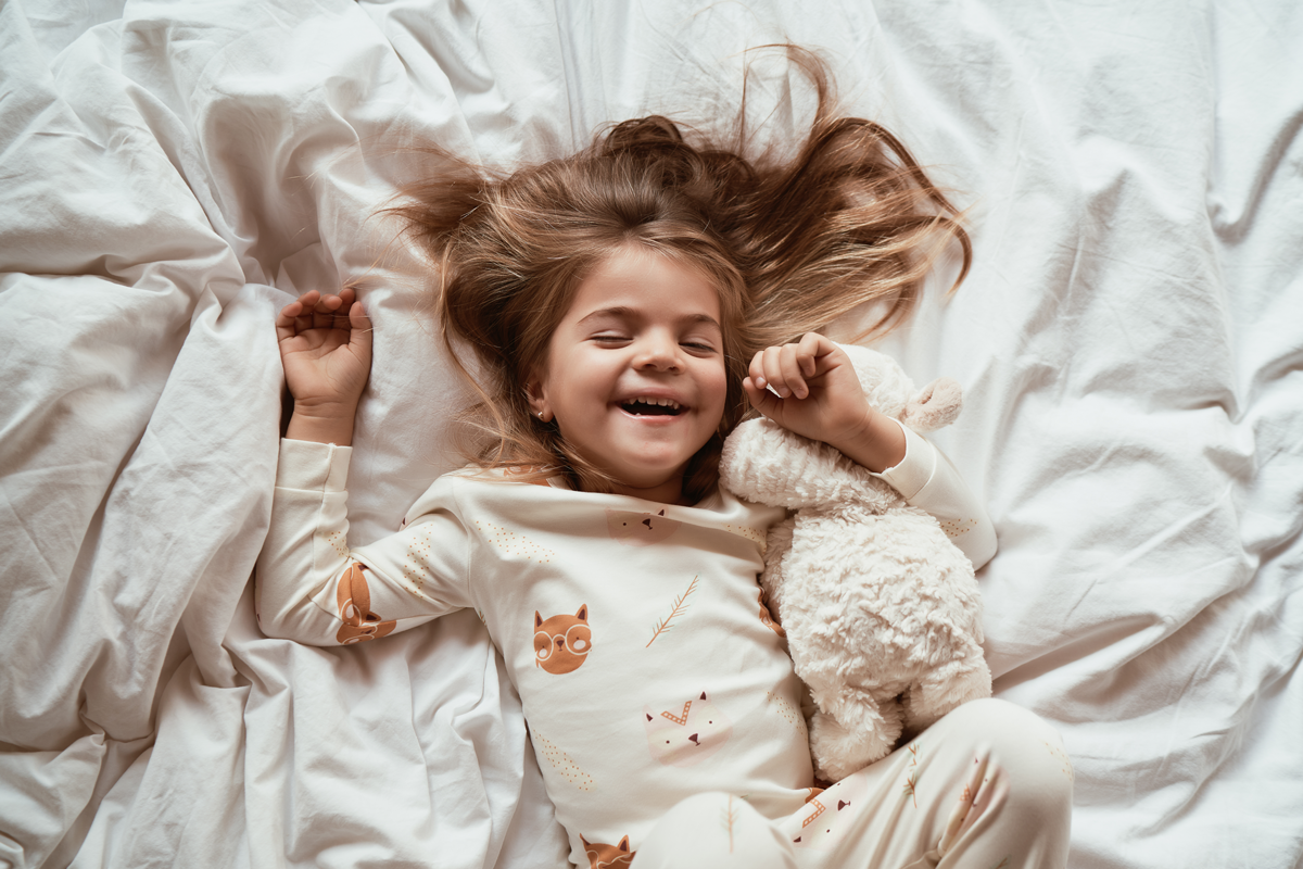 Happy Smiling Child in Comfortable Cozy Boho Children Pajamas lying on covers